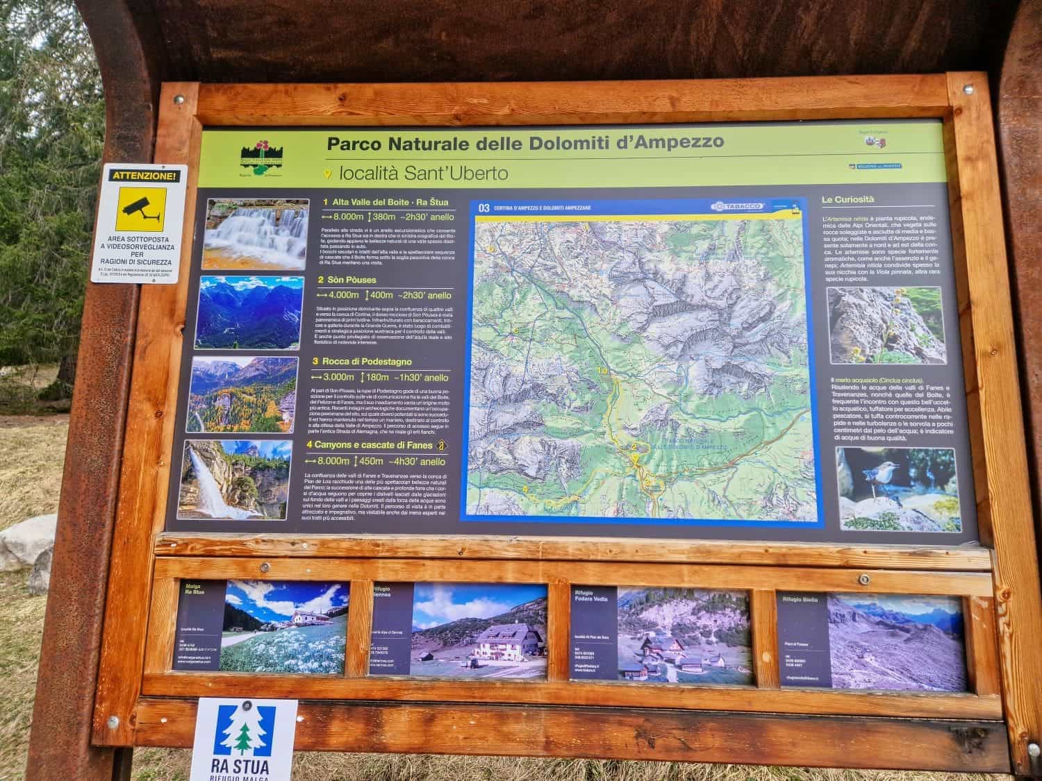 Dolomites In April: Perfect 2-Day Itinerary + What To Expect 28 Information board at Parco Naturale delle Dolomiti d'Ampezzo, locality Sant’Uberto. It features maps, hiking routes, and local regulations. Below are smaller images of park views. The sign is wooden with a natural background.
