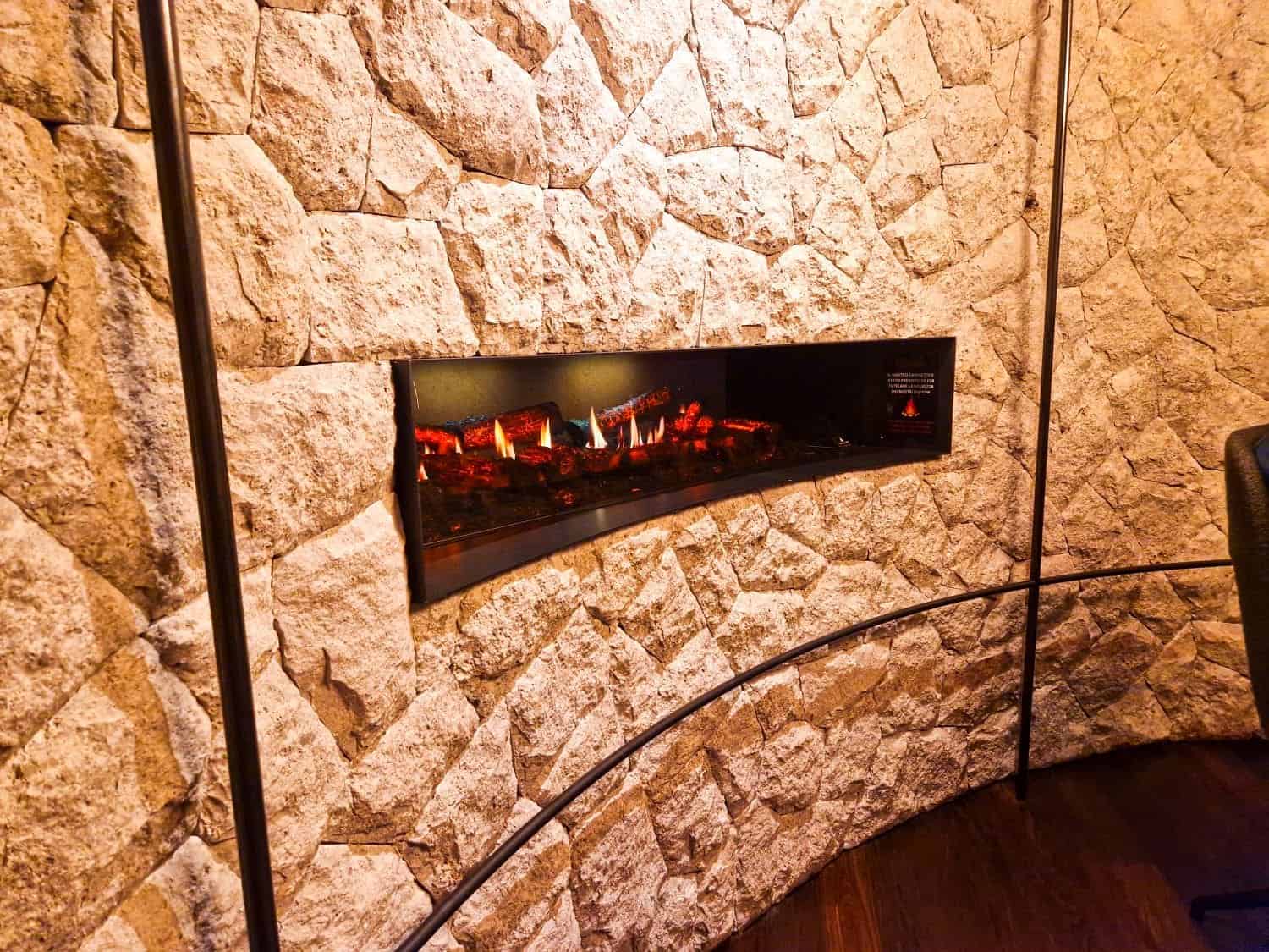 Easy Dolomites Hiking Itinerary: 5 days in Cortina d’Ampezzo 39 Modern electric fireplace set in a curved stone wall, displaying realistic glowing embers and faux logs. The surrounding stones are textured and light-colored, adding a rustic contrast to the sleek design of the fireplace.