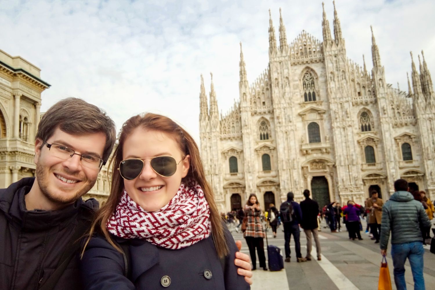 How to Get to Cortina d’Ampezzo From Key Destinations 6 A smiling couple takes a selfie in front of the Milan Cathedral in Italy. The ornate, Gothic-style facade of the cathedral is visible, with people walking and gathering in the plaza.