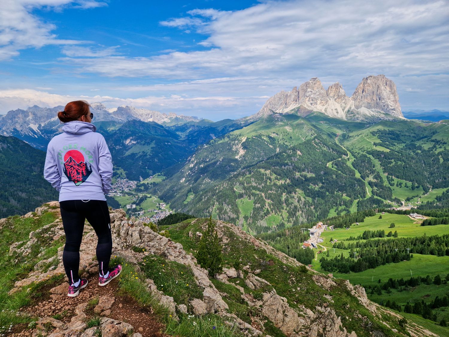 Best Dolomites Hiking Shoes: Boots, Trail runners, other? 4 A hiker stands on a rocky viewpoint overlooking the green valleys and dramatic peaks of the Dolomites near Val Gardena. The rugged mountain terrain highlights the type of landscape where the best hiking shoes for the Dolomites provide comfort, grip, and stability on uneven trails.