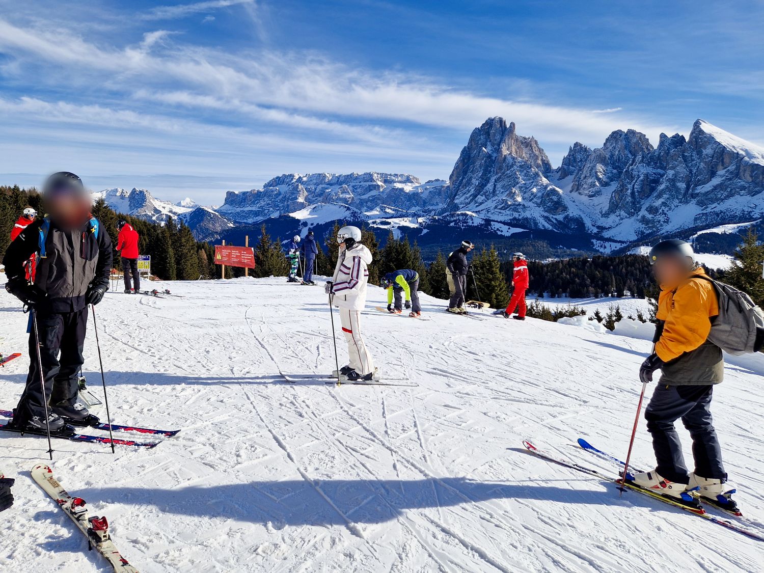 Where to stay in the Dolomites for skiing 2 Skiers gather on the snow covered slopes of Alpe di Siusi near the upper station of the Mont Seuc cable car from Ortisei in early December. The jagged peaks of the Sassolungo mountain group rise in the background beneath a bright blue sky at the beginning of the winter ski season.